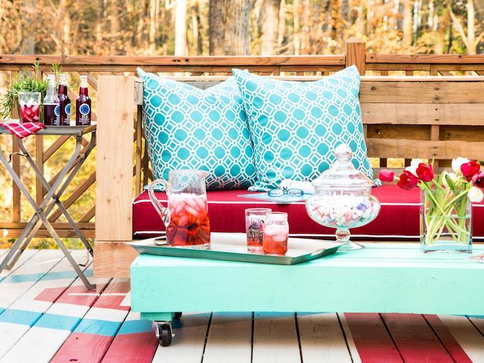 Kırmızı koltuk minderli ahşap bir kanepe, mavi dekoratif minderler ve tekerleklerle maviye yeniden boyanmış paletli bir sehpa ile palet içinde bahçe mobilyası örneği, deco teras