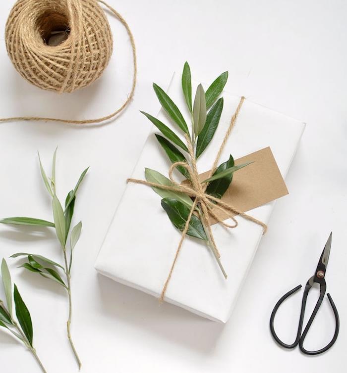 Božična darilna škatla, zavita v beli papir, zelene veje in etiketo iz kraft papirja kot okras