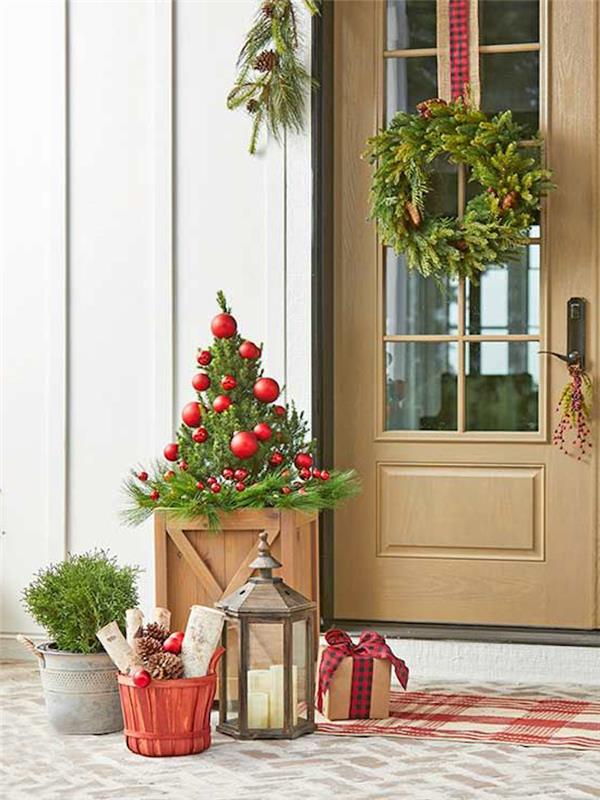 bir tencerede bir Noel ağacının önündeki fenerde bir mum ve kapıda bir çelenk ile parlak bir dış mekan Noel dekorasyonu nasıl yapılır