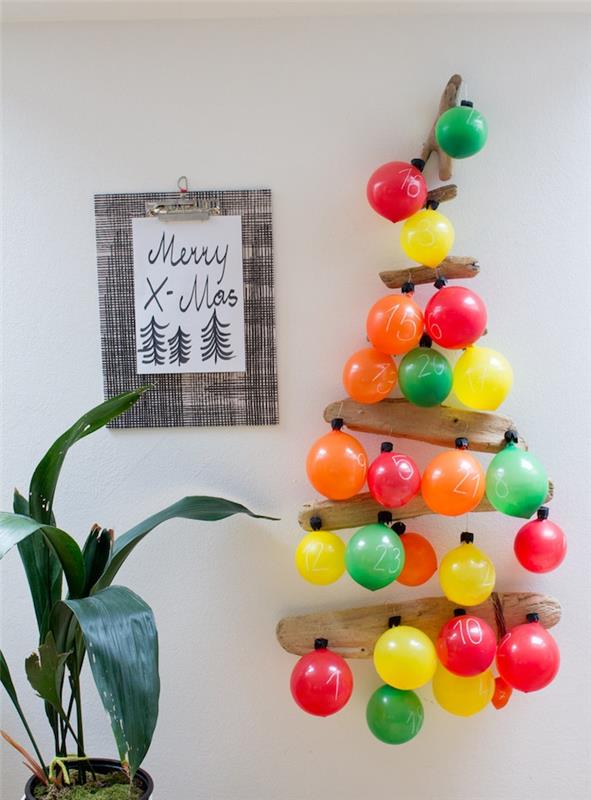 originali dreifuojančio medžio Kalėdų eglutė ir sunumeruoti bei spalvoti balionai baltos sienos fone, originalus advento kalendorius