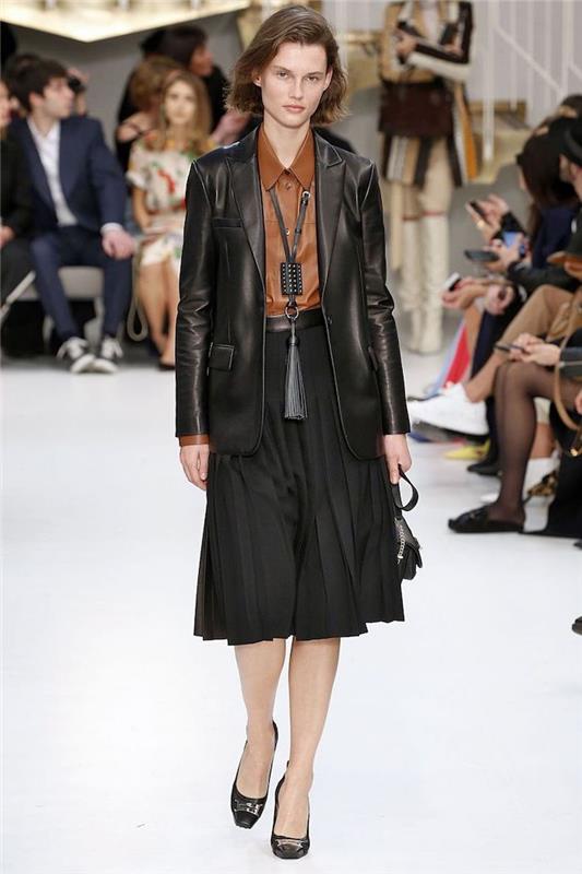 manekenka, ki hodi po vzletno -pristajalni stezi, oblečena v črno karirano krilo in blazer, novi modni trendi, rjava usnjena majica in črne pete