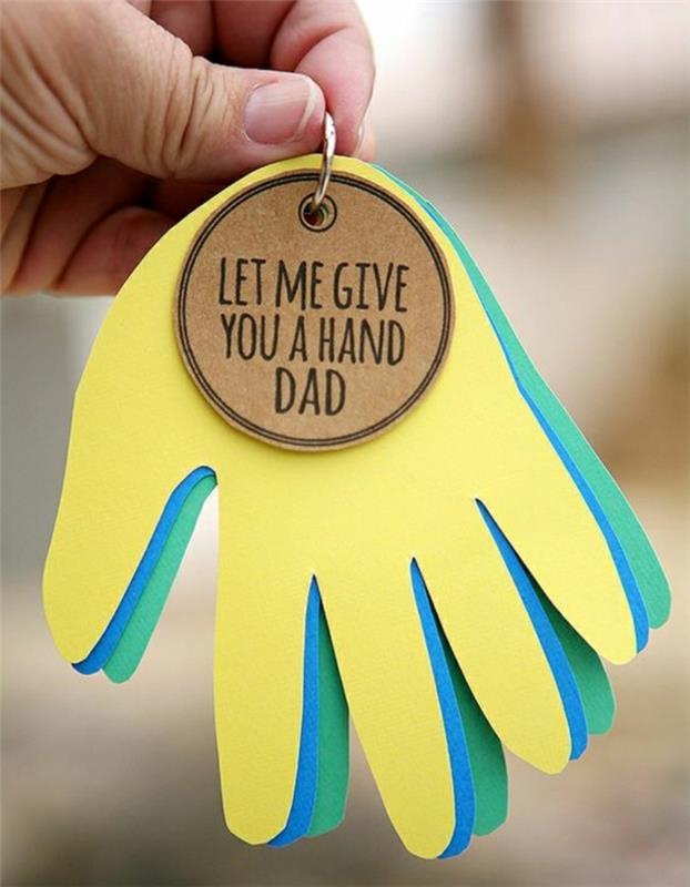 popieriniai vaiko rankos išpjovai geltonos, mėlynos ir žalios spalvos, laikomi raktų pakabuku, su šviesiai ruda etikete, laikoma už vyro rankos