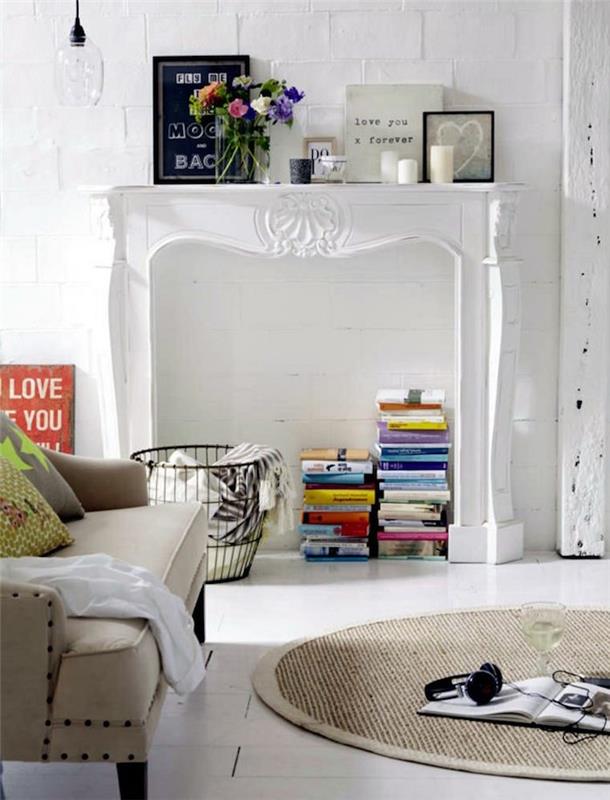 baltas medinis židinio rėmo židinys gyvenamojo kambario dekoravimui ant baltos akmeninės sienos su dekoratyvinėmis knygomis intarpe ir nuotraukų rėmeliais skandinaviškai atmosferai