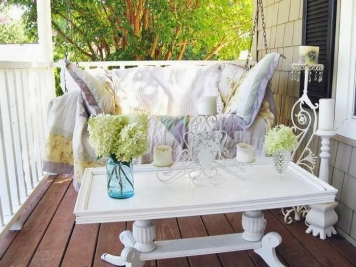 viseči stol, okrašen z blazinami in karirano ploščo, bela nizka balkonska miza, originalni svečnik in vaze s cvetjem