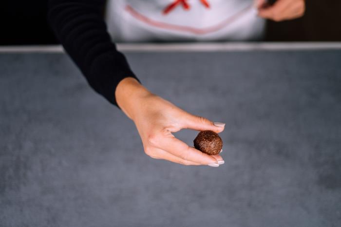 granitna plošča, proteinske kroglice iz arašidovega masla, ženske roke, s sivim lakom za nohte, ki čokolado oblikujejo v kroglo