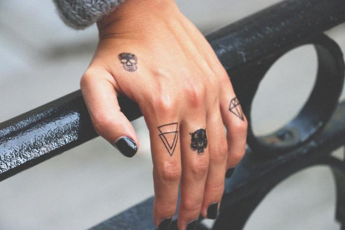 mažos tatuiruotės ant pirštų, vaizduojančios kaukolę, du trikampiai, tigro galva ir mini deimanto tatuiruotė