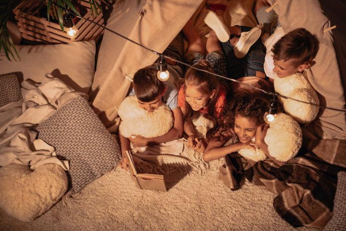 Üzerinde hafif bir çelenk bulunan bir çadırda orijinal bir pijama partisi, çocuklar toplu okuma yapıyor