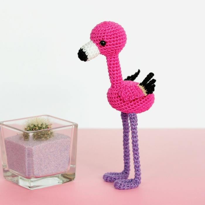 majhna pletena otroška igrača v obliki flaminga, okras flaminga, figura, postavljena v bližini steklenega kozarca s peskom in kaktusom