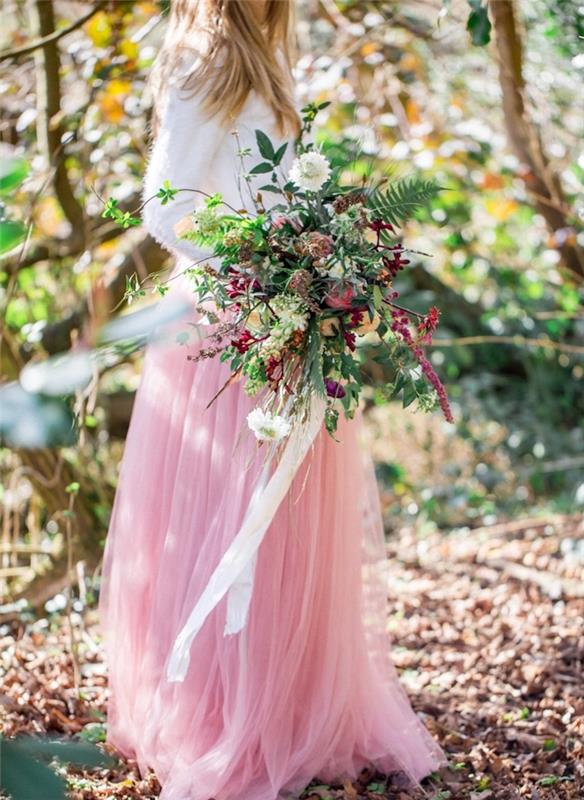šalies vestuvių gėlių pavyzdys, spalvinga puokštė, moteris baltu viršumi ir rožiniu sijonu, miško rėmas
