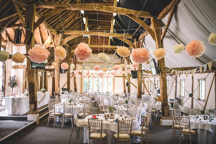podeželska elegantna poroka v hlevu, obešeno belo in rožnato cvetje iz papirnatega papirja, izpostavljeni tramovi, mize preprosta dekoracija