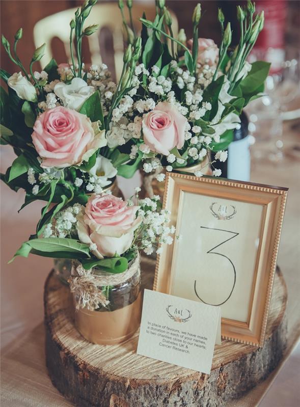 vestuvių stalo deko, kaimo stilius, „pasidaryk pats“ vestuvių idėja, medinis rąstas, su nudažytu aukso spalvos stikliniu indeliu, rožių ir pakalnučių puokštė, auksinis rėmas, stalo numeris