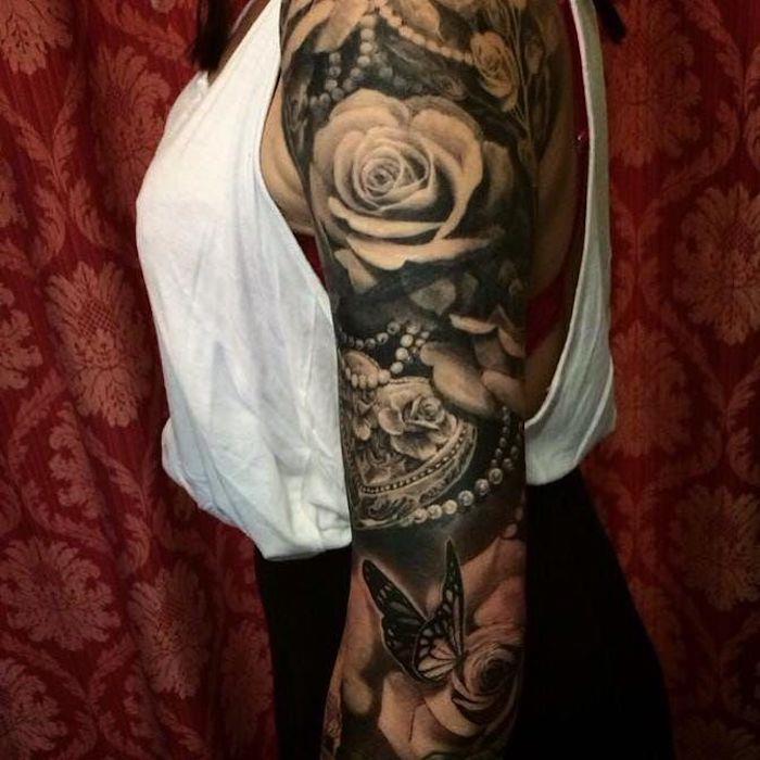 tetovaža na roki ženske vrtnice in ogrlice, metulj, rožnato cvetje, bela brezrokavnica, črno -bela ideja za tetoviranje