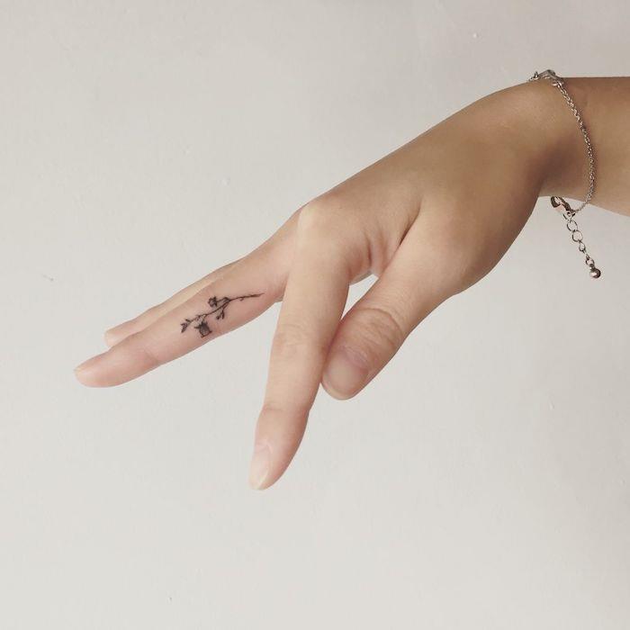 majhen cvet, tetovaža s srednjim prstom, tetovaža s prekrižanimi prsti, roka pred belim ozadjem, s srebrno zapestnico