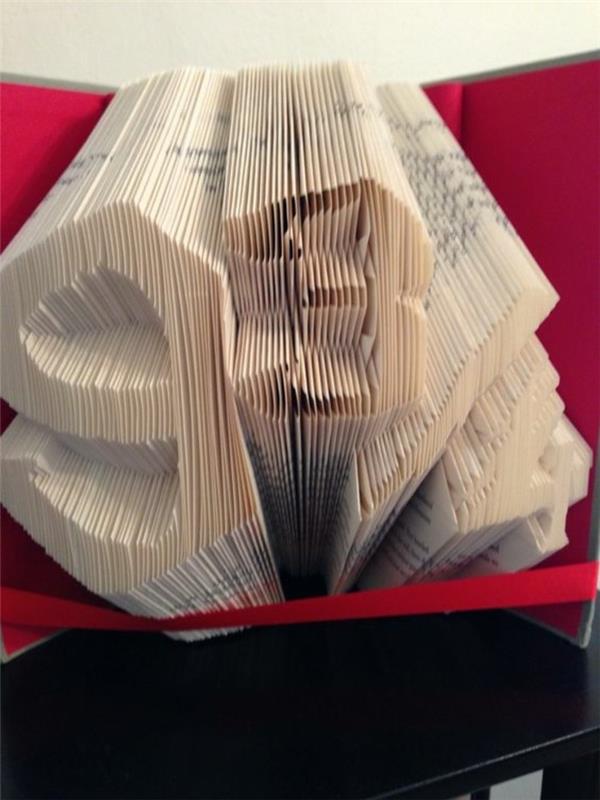 zložena knjižna umetnost, knjiga s trdimi rdečimi platnicami, okrašena z rdečim trakom in odprta za prikaz številk 9 3/4, narejena iz prepognjenih strani