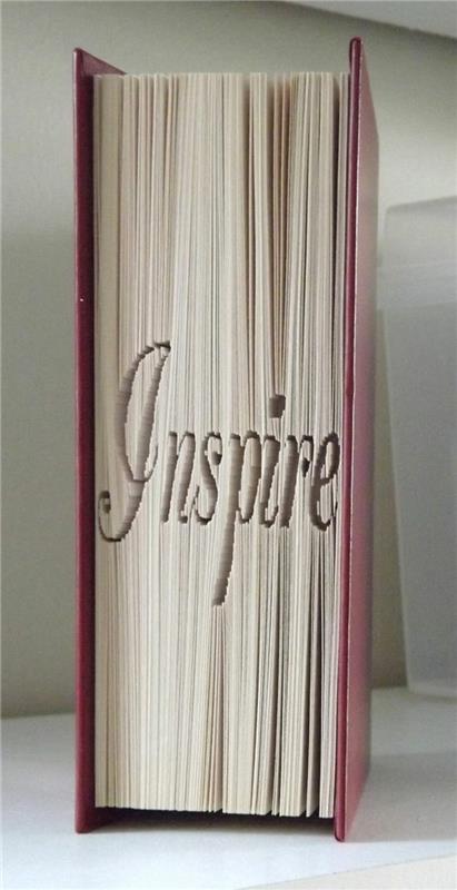 zložena knjižna umetnost, zaprta knjiga s trdo vijoličnimi platnicami, zložene strani, ki črkujejo besedo navdih, v domišljijskem pisanju
