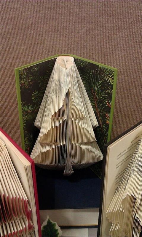 zloženi knjižni umetniški vzorci, majhno božično drevo, narejeno iz prepognjenih strani, znotraj odprte knjige, s trdimi zelenimi platnicami in vzorcem borovega drevesa, več podobnih knjig v bližini
