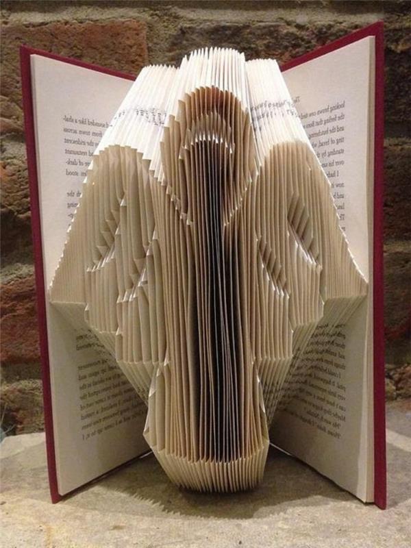 zloženi vzorci knjig, preproste oblike angela, narejeni iz prepognjenih strani, znotraj odprte knjige, z rdečimi trdimi platnicami