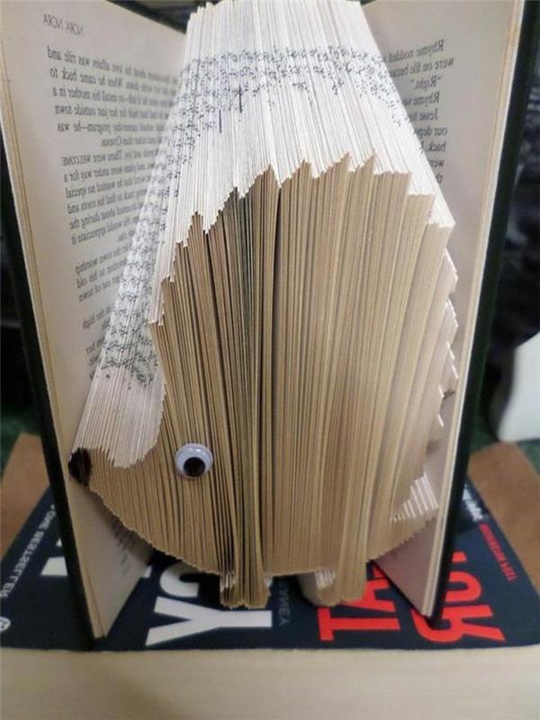 zloženi vzorci knjig, knjiga s črnimi trdimi platnicami, odprta, da razkrije obliko ježa, narejena iz prepognjenih strani, okrašena s črnim markerjem in nalepljenim očesom