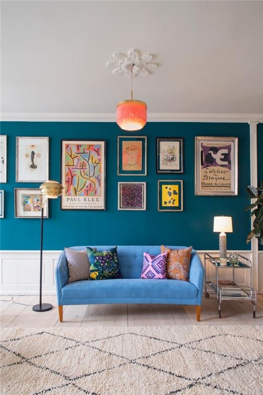 Neşeli tonlarda bir fotoğraf galerisi ve turkuaz mavisi tonunda bir kanepe ile zenginleştirilmiş ördek mavisi duvar