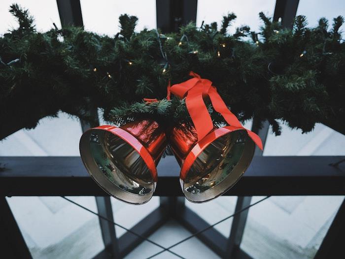 Kalėdų fonas raudonuose kalėdiniuose varpuose, papuoštuose paprasta juostele ir pušies šakų girlianda su lengva girlianda