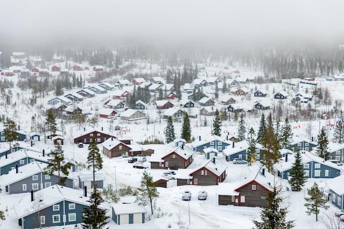 žieminiai tapetai, snieguotas kaimas Švedijos kalno papėdėje, mėlyni, rudi ir raudoni nameliai