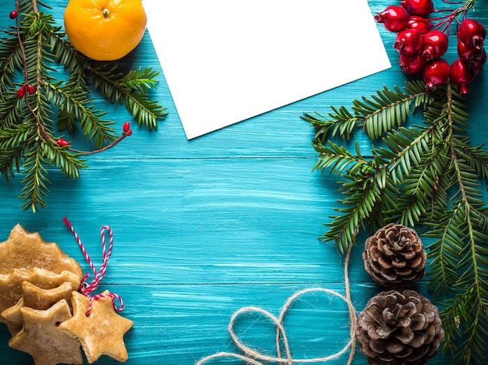 paprasti kalėdiniai tapetai, pagaminti iš pušies šakų, sausainių, kankorėžių, holijos, oranžinės ir baltos spalvos lapų mėlyname fone