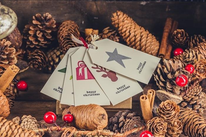 kalėdiniai tapetai su kankorėžiais, cinamonu, holija ir dovanų etiketėmis ant medinio stalo