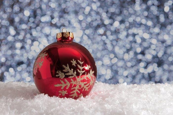 paprasta kalėdinių tapetų idėja raudoname kalėdiniame baliuje, dekoruotame blizgančia sniego kolba, dirbtiniu sniegu
