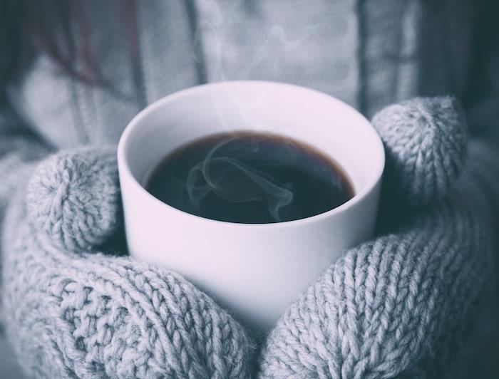 žieminiai tapetai baltame kavos puodelyje, pirštinės ir pilkas megztinis, kokono įvaizdžio idėja, hygge