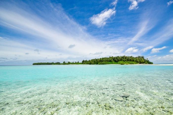sala Indijos vandenyne, rožinis žalios ir turkio spalvos kraštovaizdis, saulė spindintis dangus su debesimis, kurie atrodo kaip subtilios užuolaidos
