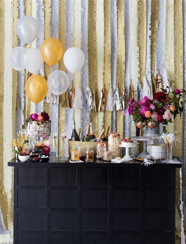 novoletna sladkarija s kozarci, steklenicami šampanjca, šopkom rož in novoletno torto, balonom devo in venci na ozadju