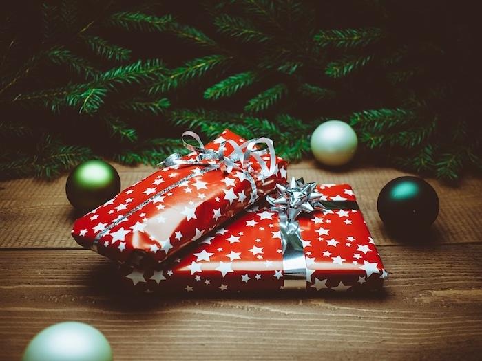 Kalėdų tapetai, dovana su raudonu įvyniojimu su baltomis žvaigždutėmis, žaliomis pušies šakomis ir žaliais kalėdiniais kamuoliukais ant medinio paviršiaus