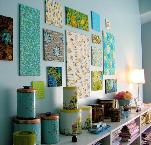 Bir odanın mavi duvarı, çok sayıda farklı boyutta tuval, çeşitli, çok renkli desenlerle dekore edilmiş, yakınlarda birçok farklı eşya bulunan raf