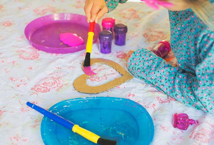 linksmi užsiėmimai vaikams patalpose, mėlynos ir rožinės spalvos plastikinės lėkštės, dažai viduje, mergina piešia širdį