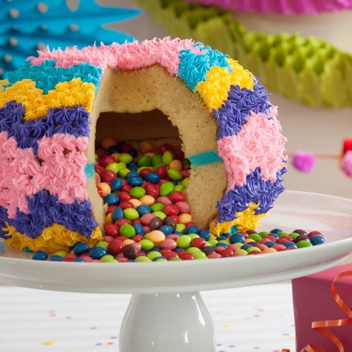pinata torta v obliki krogle z votlim središčem, napolnjenim s sladkarijami, z barvno glazuro, narejeno z dekorativno slaščičarsko vrečko