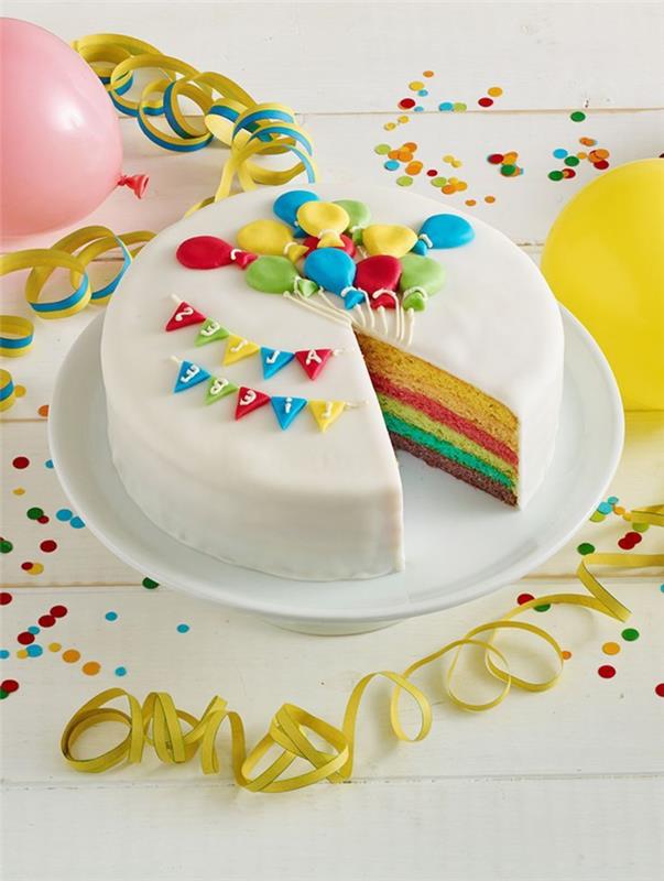 mielas vaivorykštinis pyragas, padengtas baltu fondantu ir dekoruotas balionais ir girliandomis, imituojamomis cukraus pasta