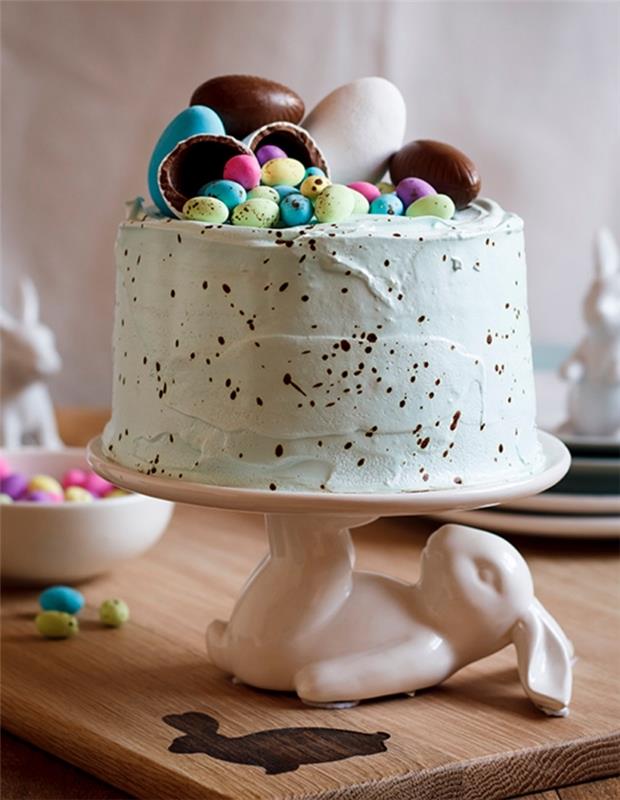 pestra velikonočna gnezdna torta s pastelno zeleno obarvano masleno kremo, okrašena s čokoladnimi jajci, postavljena na simpatično stojalo za zajčjo torto