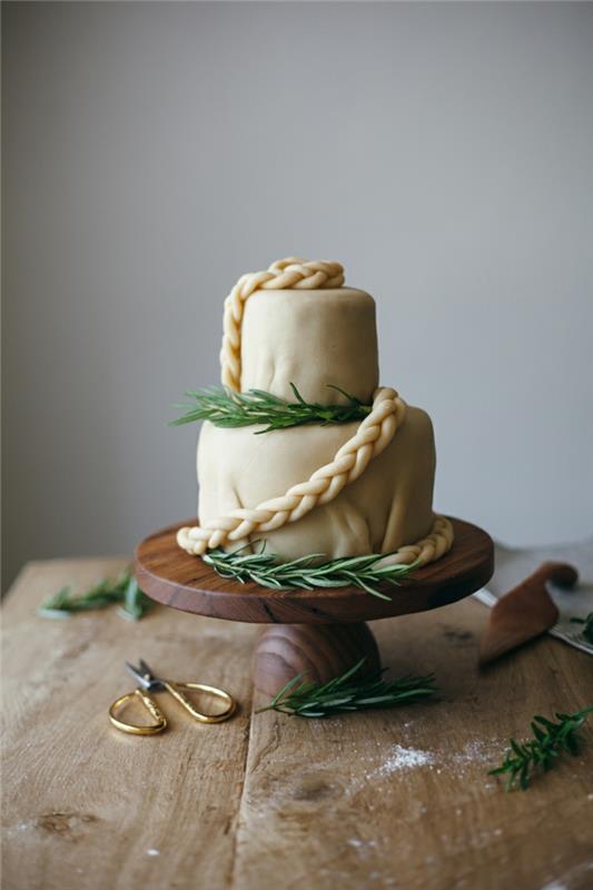 itin elegantiškas baltas vestuvių tortas, medinis stalas, žirklės su auksinėmis rankenomis, pušies šakelių apdaila