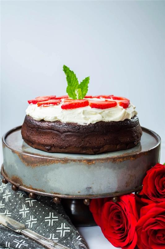 izviren recept za čokoladno torto brez moke, prelito s stepeno smetano in okrašeno z narezanimi jagodami
