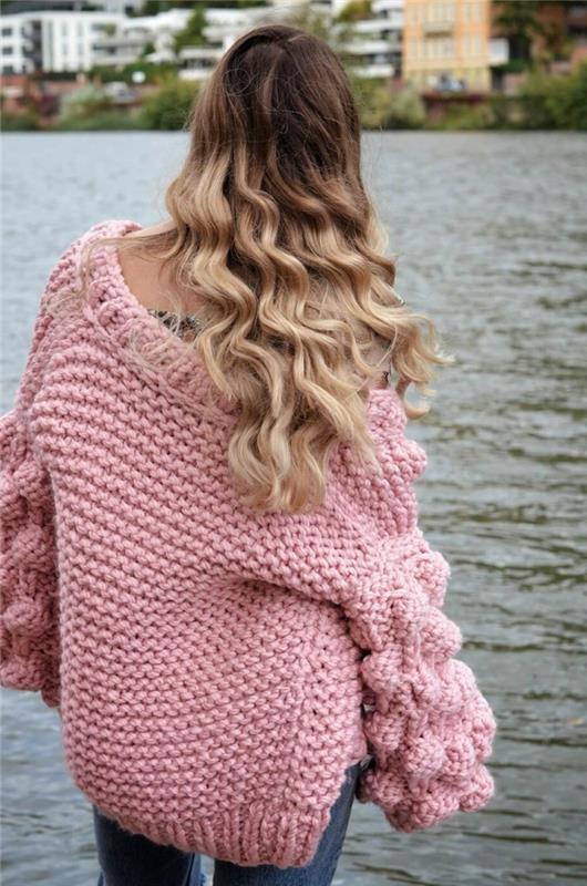 negabaritinis rožinis moteriškas megztinis, originalios rankovės, didelis megztas megztinis, kurį dėvėjo šviesiaplaukė moteris prie upės