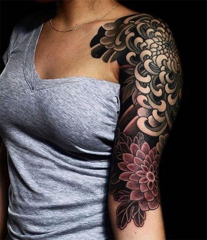 ženska tetovaža z roko in ramo, siva majica, tetovaža cvetja dalije, subtilna ogrlica, črno -rdeča tetovaža