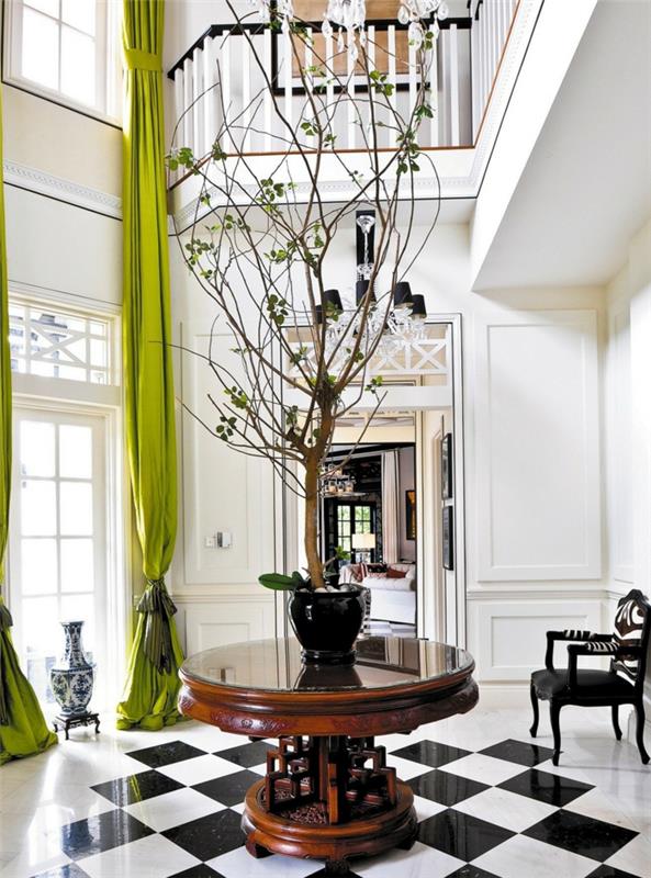 baltas įėjimas, didelis langas ir žalios užuolaidos, mažas apvalus stalas su dekoratyviniu medžiu, languotos plytelės, barokinė kėdė