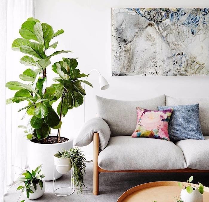 namestite velik cvetlični lonec v kotu sobe, leseni kavč s sivo blazino, stensko dekoracijo abstraktnega umetniškega okvirja, okroglo mizico