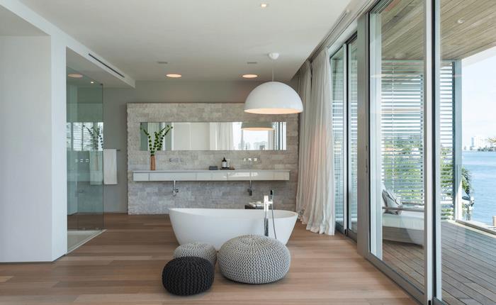 Yumurta banyosunun tepesinde dev avize, parke zeminde tabureler, deniz manzarası, beyaz ve ahşap banyo, banyo tezgahı