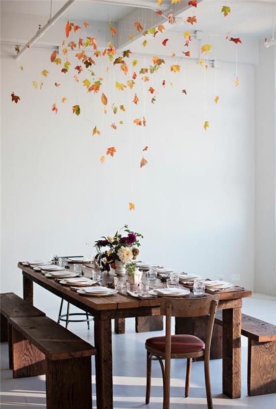 papuoštas valgomasis stalas, baltos lėkštės ant tamsaus medinio stalo, centrinė vazos dalis, vainikas rudens lapuose