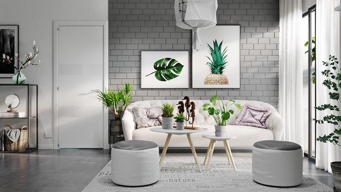 balta siena su pilkomis plytomis, šviesiai kreminė sofa, svetainės spalvų idėjos, keli vazoniniai augalai ir du dideli, įrėminti botanikos kūriniai, kokios spalvos atrodo gerai su pilka spalva