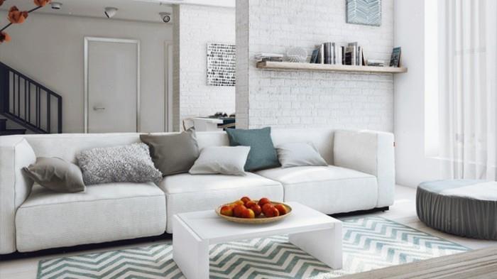 mažas baltas kavos staliukas, pilkos svetainės sienos, baltos plytos siena, balta sofa, mėlynos ir smėlio spalvos pagalvės