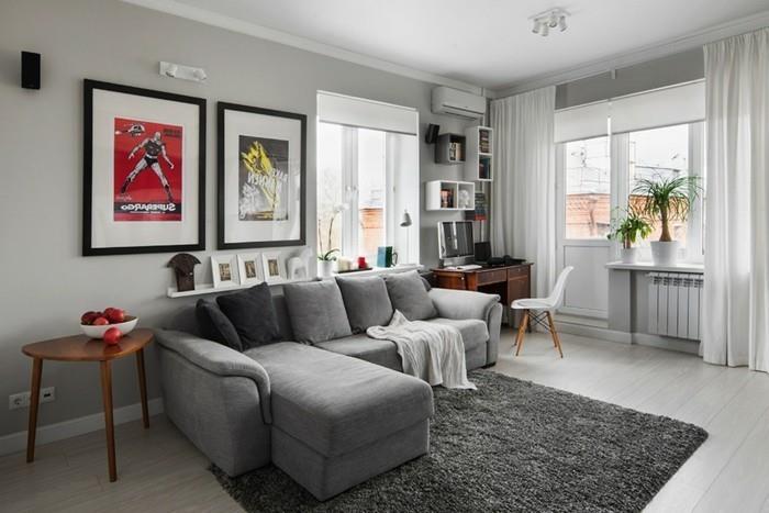 pilka kampinė sofa, įrėminti kabantys plakatai, medinis šoninis stalas, pilkas kilimas, medinės grindys, pilkos svetainės sienos