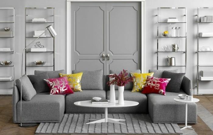pilkos svetainės sienos, pilka kampinė sofa, rožinė ir geltona, pagalvės, pilkas kilimas, baltas kavos staliukas