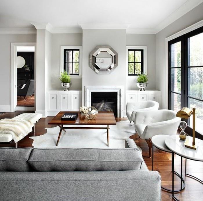 balti foteliai, veidrodis virš židinio, akcento spalvos pilkai, pilkai sofai, medinis kavos staliukas